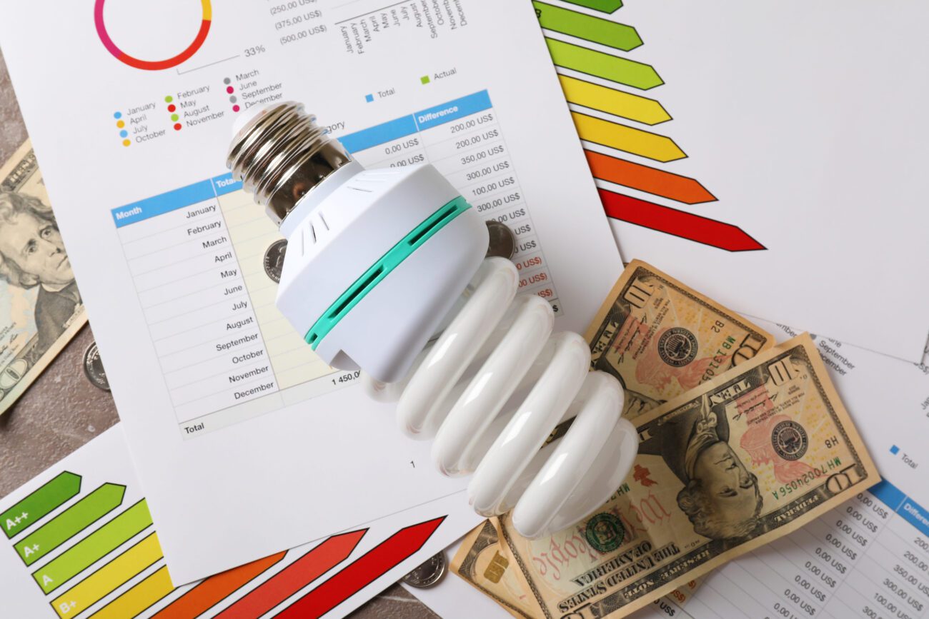 Energy saving concept top view and close up - Madrid Noticias 24h CFL light bulb atop energy charts and dollar bills, illustrating electricity costs and savings