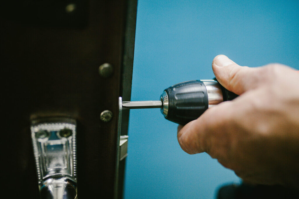 Person using a cordless drill to install a door lock into a wooden door in close-up