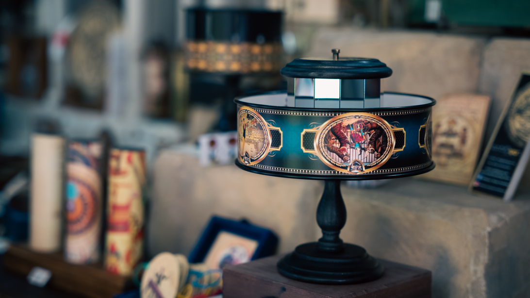 Decorative vintage table lamp with a blue-gold ornate band, displayed on a dark pedestal in a shop window/inside a store.
