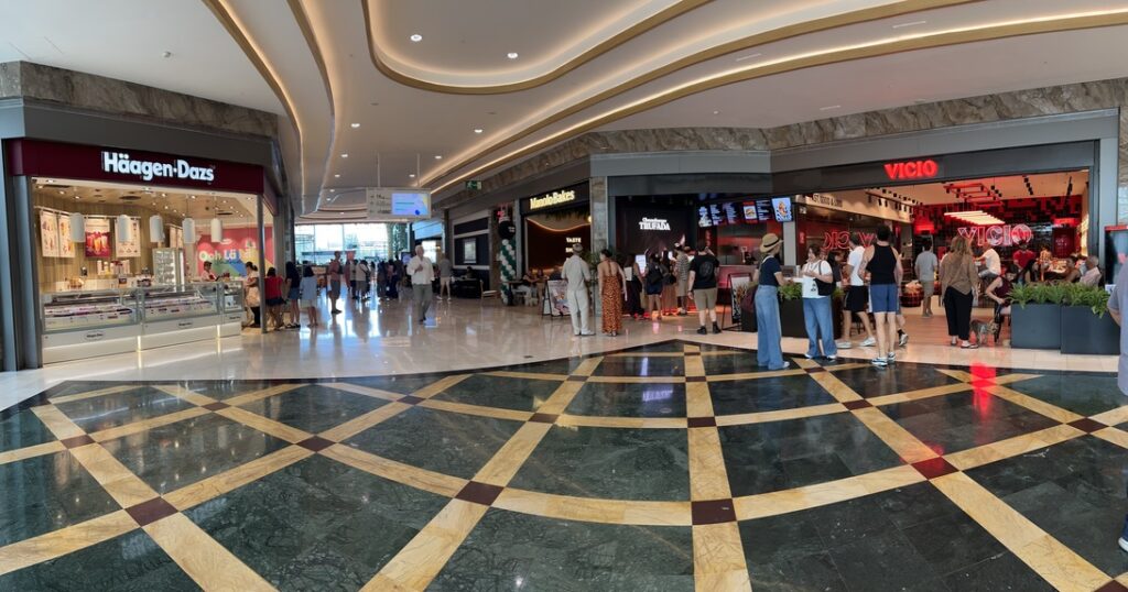 Wide mall corridor with Häagen-Dazs on the left and other eateries on the right, shoppers walking and queuing nearby.