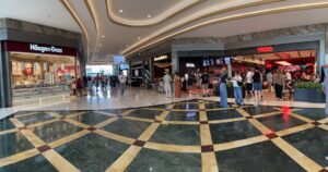 Wide mall corridor with Häagen-Dazs on the left and other eateries on the right, shoppers walking and queuing nearby.