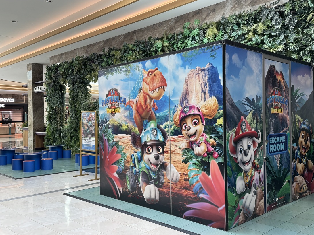 La Patrulla Canina Gran Plaza - IP - Madrid Noticias 24h Colorful wall panels featuring Paw Patrol characters in a jungle scene inside a shopping mall; an escape room sign visible on the panels.