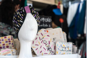 Artesania otoño Recoletos - IP - Madrid Noticias 24h Mannequin head wearing a black headwrap with colorful sprinkles pattern in a shop display of pouches with doughnut-sprinkle designs behind it